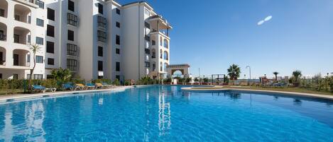 Una grande piscina con lettini e un edificio a più piani con balconi.
