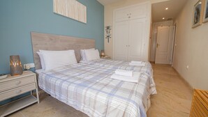 Un dormitorio con cama, mesitas de noche, una lámpara de pared y una puerta que da a otra habitación.