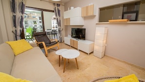 Una sala moderna con sofá, sillón y mesa de centro. Hay un televisor, armarios y una ventana con cortinas.
