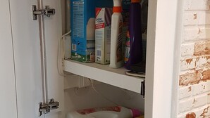 A compact laundry room with a washing machine, detergent, and cleaning supplies on shelves. - Sunny & Ocean view Apartment (Los Cristianos)