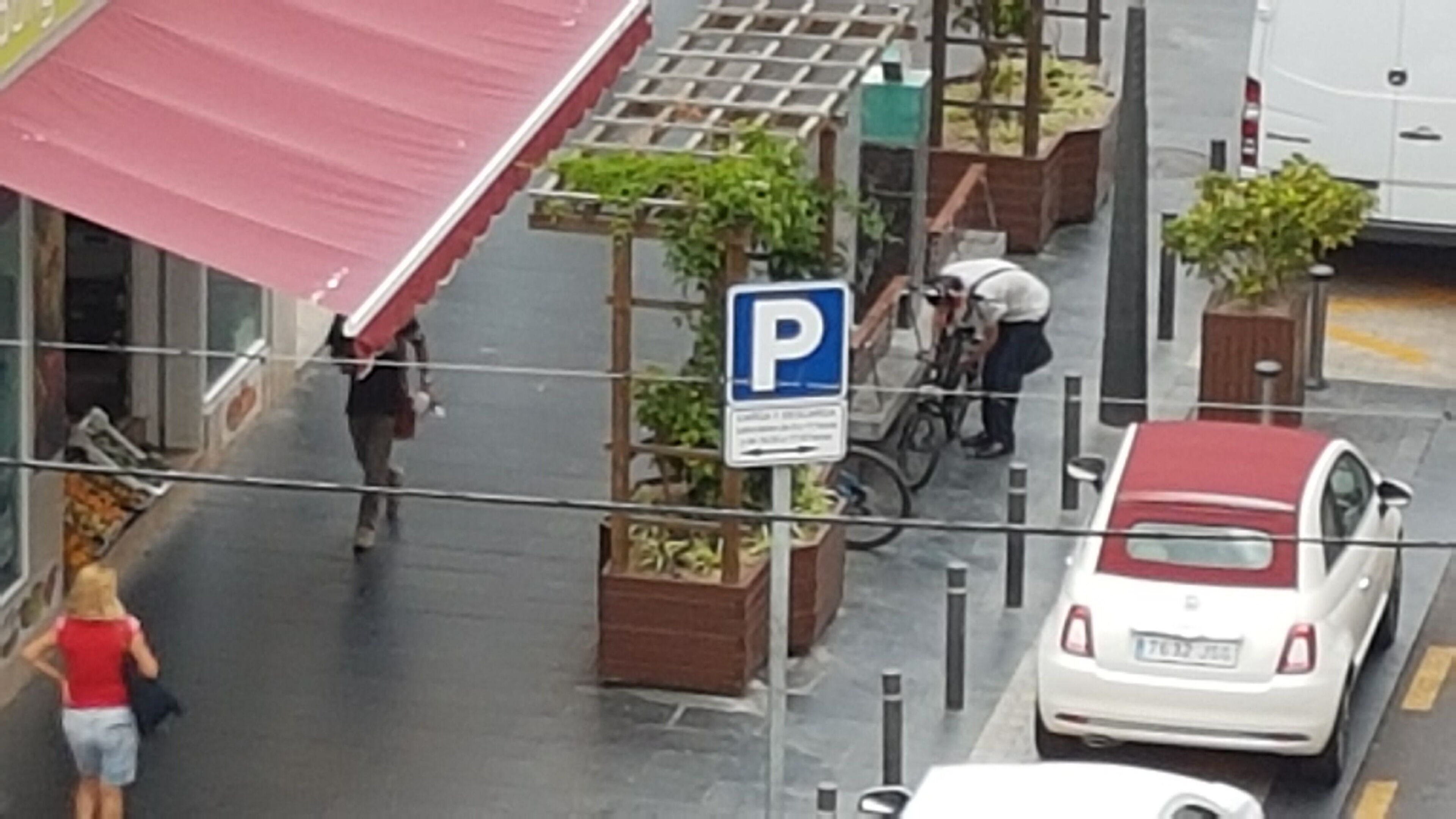 Et gadesyn med et parkeringsskilt, en hvid bil og en person med en cykel.