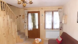 Um interior em madeira com escada, mesa de madeira, sofá marrom e janela com cortinas.