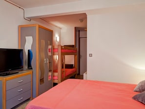 Un dormitorio con literas, un televisor sobre un mueble de madera y un armario con puertas espejadas.