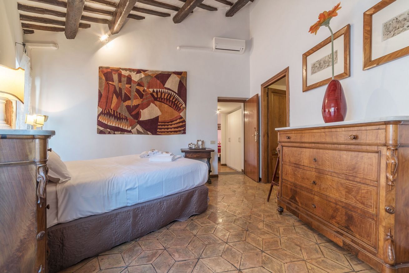 A bedroom with a bed, a wooden dresser, a wall-mounted air conditioner, and a geometric patterned artwork.