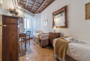 A room with two beds, a wooden wardrobe, a desk with a chair, and a mirror on the wall.