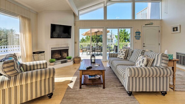 A spacious living room with a fireplace, striped sofas, a coffee table, and a TV mounted on the wall. - Westhampton Beach Home w/ Deck + Ocean Views! (Westhampton Beach)