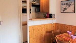 A compact kitchen with wooden cabinets, a microwave, and a kettle on a shelf. - Studio Mountain Getaway with Balcony, Parking, Near Slopes and Shops (Vars)