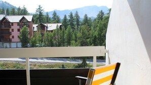 A balcony with a striped chair, overlooking a mountainous area with buildings and trees. - Studio Mountain Getaway with Balcony, Parking, Near Slopes and Shops (Vars)