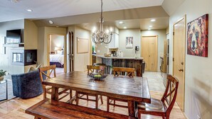 A spacious dining area with a wooden table and chairs, a chandelier, and a kitchen in the background. - Purgatory Resort Condo, Walk to the Chairlift (Durango)