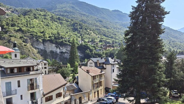Um hotel com vista para uma paisagem montanhosa, carros estacionados e uma rua com edifícios.