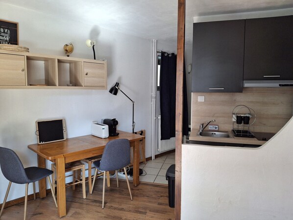 Una cocina compacta con una mesa de madera, sillas, una pequeña encimera y un cubo de basura negro.