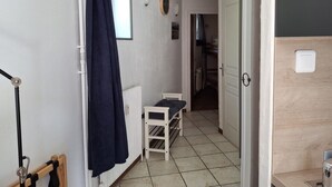 Um corredor estreito com um radiador branco, uma porta branca e uma pequena mesa branca com uma almofada escura.