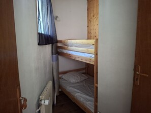 Una habitación pequeña con una cama litera, un radiador, una puerta y una ventana con cortina.