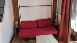 Quarto com um sofá vermelho, uma pequena mesa de madeira e duas luminárias de cabeceira.