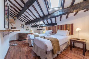 A bedroom with two beds, wooden beams, a hanging light, and a bedside table.