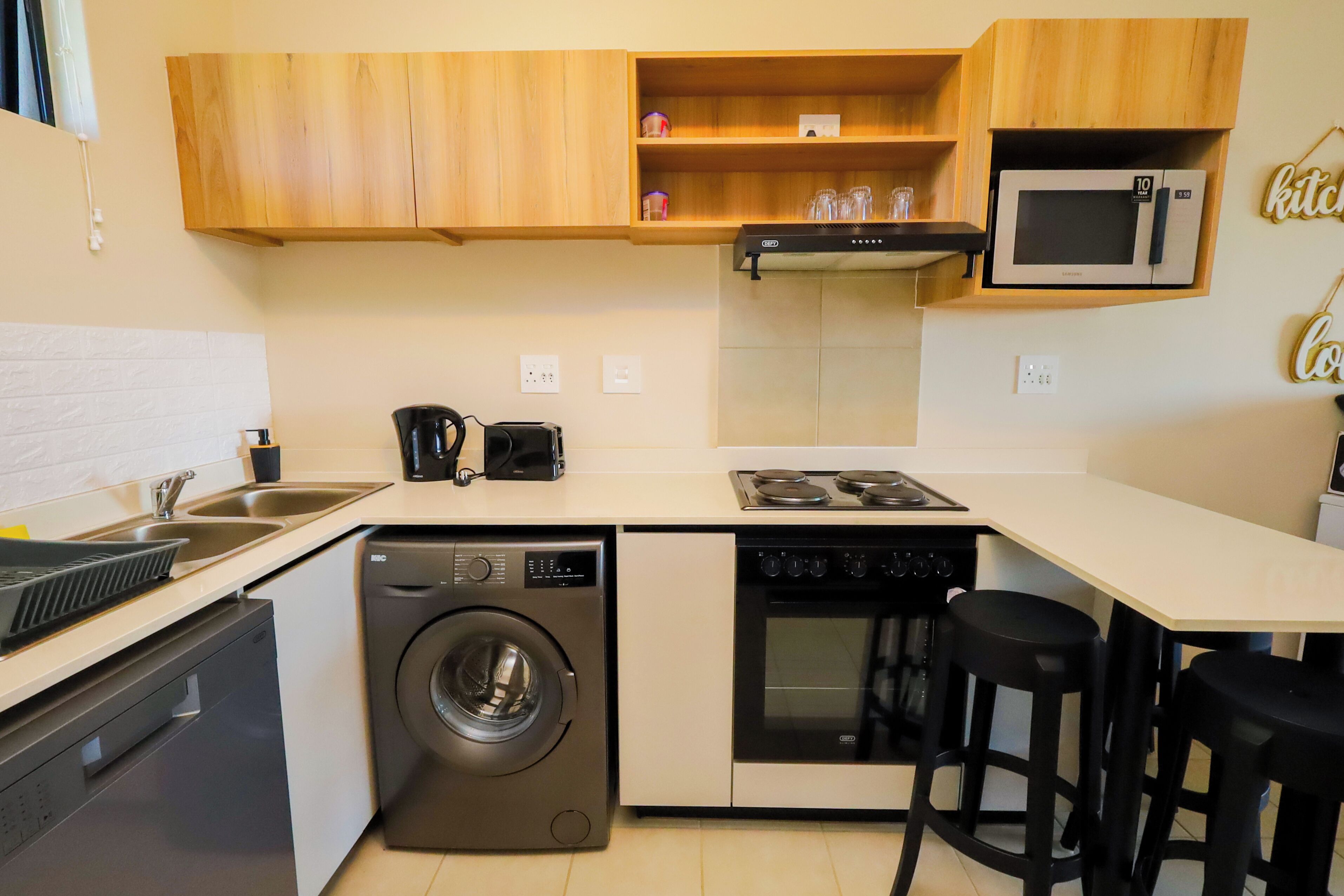 A compact kitchen with a washing machine, oven, microwave, and a coffee maker.