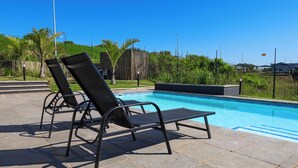 Zona junto a la piscina con dos sillas de descanso y vista despejada al agua.