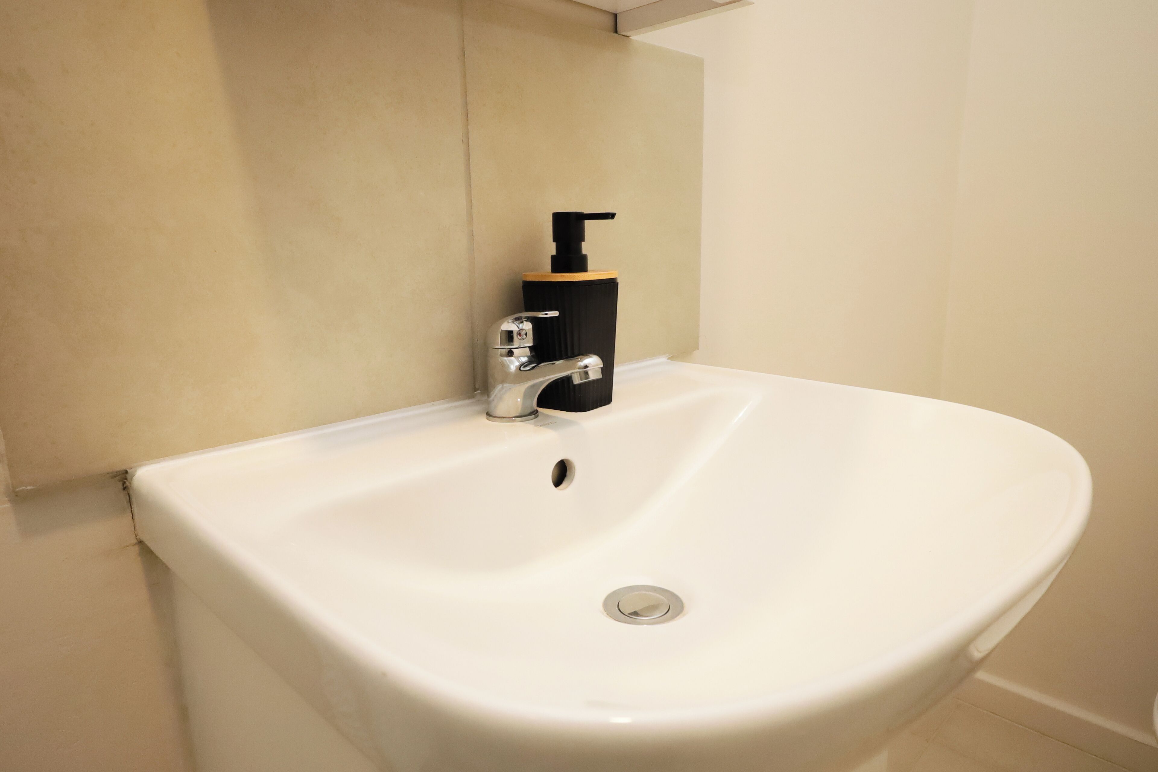 A white bathroom sink with a black soap dispenser and a chrome faucet.