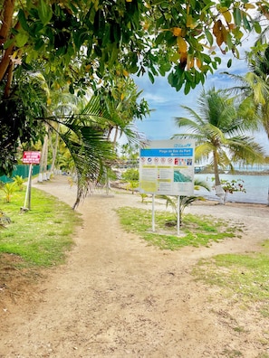 A beach path leading to a signboard with information about Plage de Bas Fort, including safety warnings and beach activities.