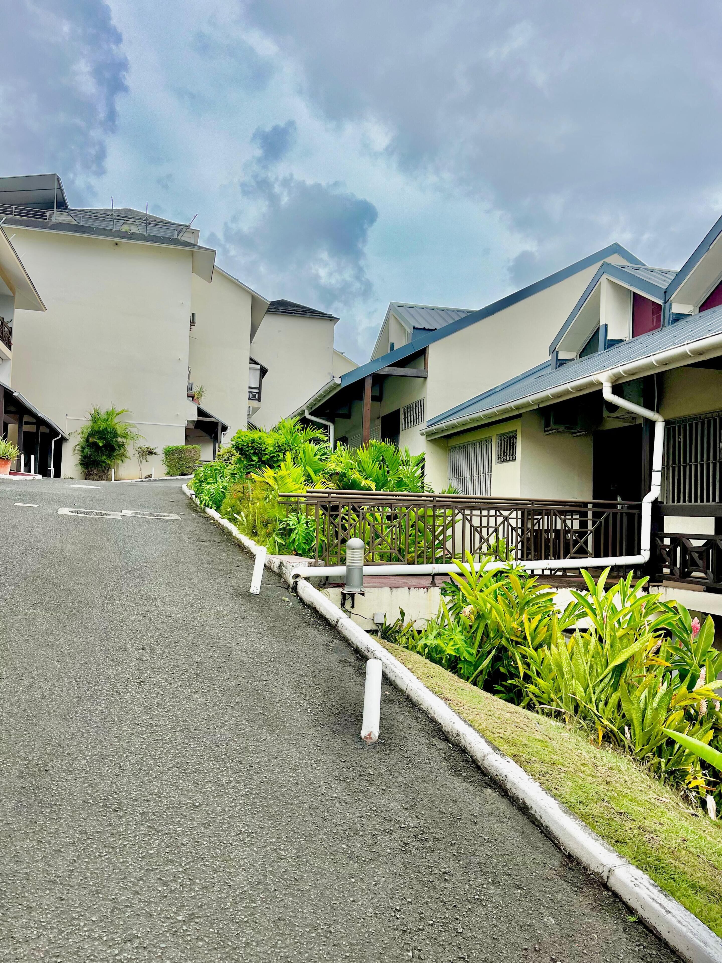 A residential street with houses, a paved road, and greenery.
