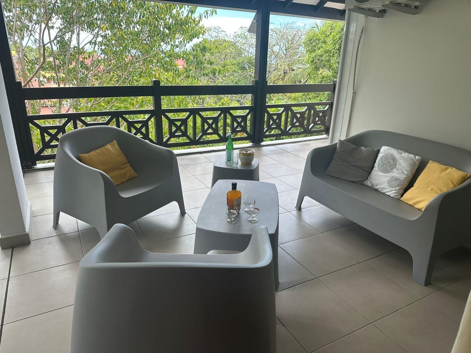 A balcony with a grey sofa, a grey armchair, and a small table with a bottle and glasses.