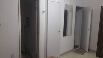 A hallway with white walls, a tiled floor, and a door with a mirror.