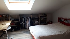 Um quarto em dormitório com claraboia, uma cama, uma escrivaninha e um guarda-roupa.