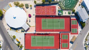 An aerial view of a sports complex with multiple tennis courts, a basketball court, and a large white dome structure.
