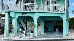A turquoise two-story building with a covered porch, a visible address sign, and a staircase leading to the upper level.
