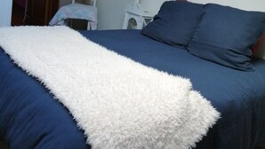 A bedroom with a bed, a white fluffy throw, a red lamp, and a painting on the wall.