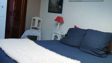 A bedroom with a bed, a white fluffy throw, a red lamp, and a painting on the wall.