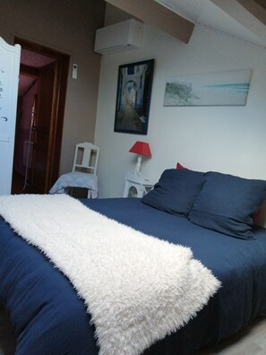 Een slaapkamer met een bed, een zachte witte plaid, een rode lamp en een schilderij aan de muur.