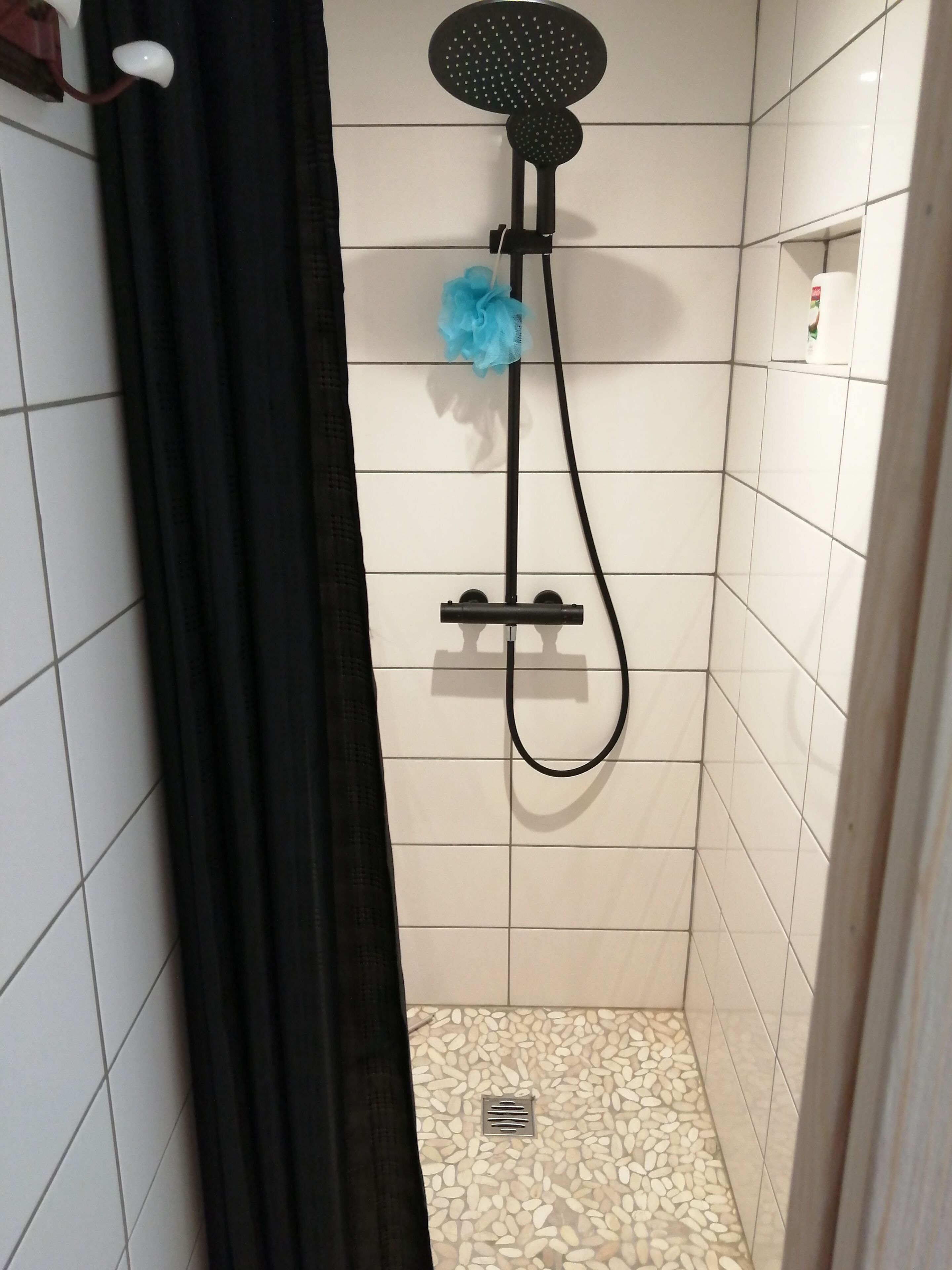 A shower with a handheld showerhead, a black curtain, and a tiled floor.
