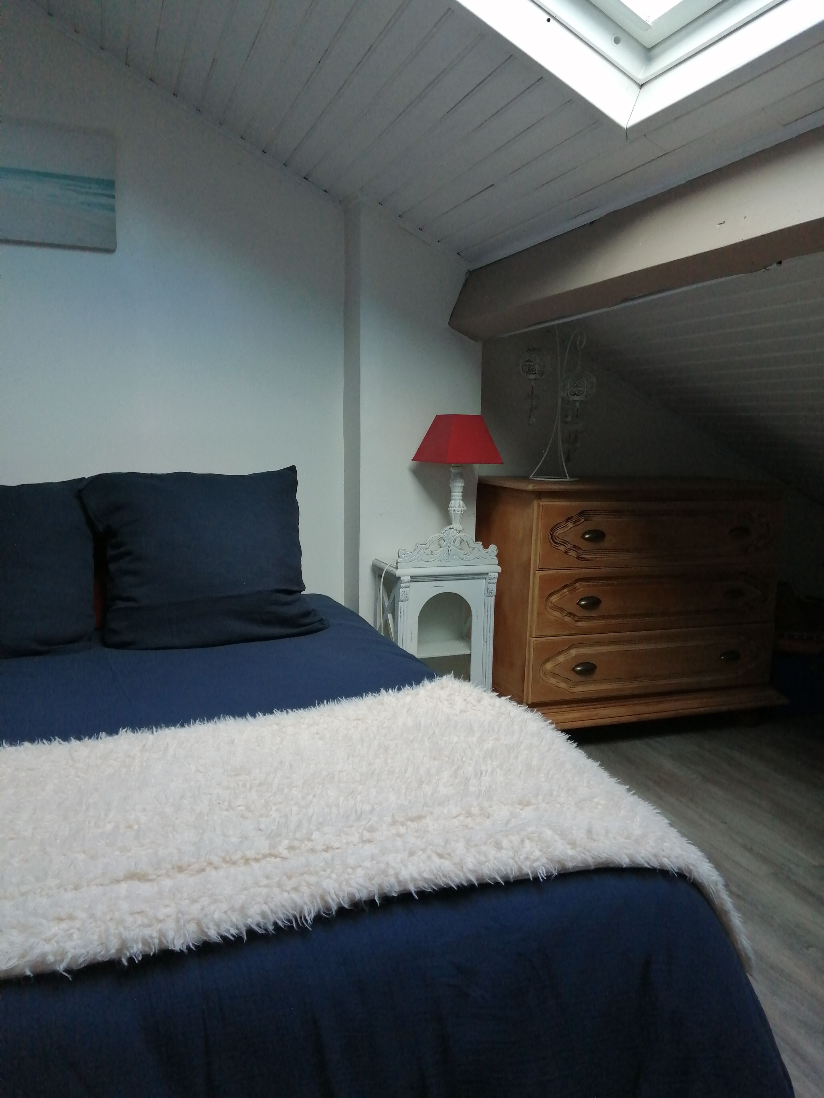 A bedroom with a bed, a dresser, a lamp, and a skylight.