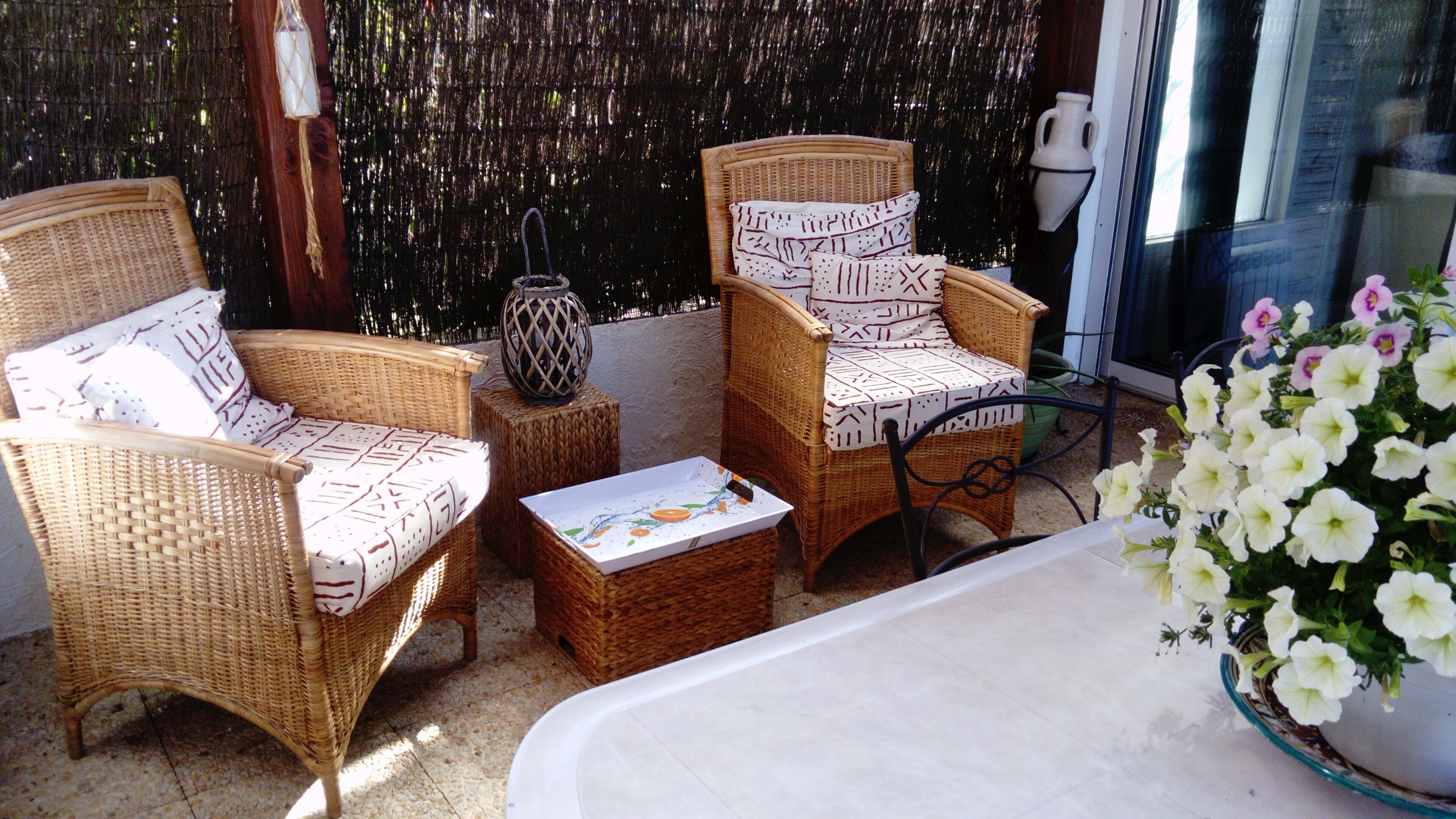 A wicker chair set with patterned cushions, a small table with a box, and a potted plant with white flowers.