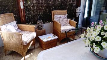 A wicker chair set with patterned cushions, a small table with a box, and a potted plant with white flowers.