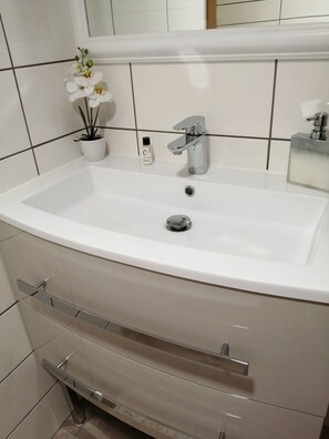 Een badkamer met een witte wastafel, een spiegel erboven, een potorkidee en een fles handzeep.