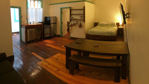 A compact room with a kitchenette, a bed, and a wooden table.