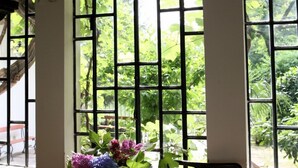 Una habitación con un gran ventanal de diseño cuadriculado, una silla y una mesa con un jarrón de flores.