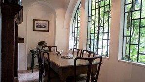 Un comedor con una mesa y sillas de madera, ventanas amplias con vistas a la vegetación y un cuadro enmarcado en la pared.