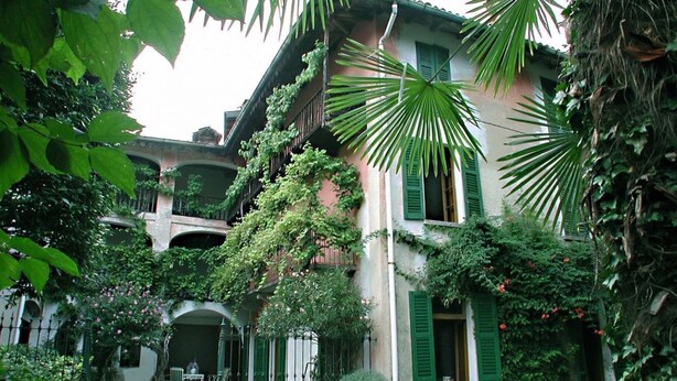 Un patio con un edificio que tiene contraventanas verdes y un porche cubierto.