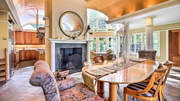A spacious dining area with a large wooden table and chairs, a fireplace, and a view of the outdoors through large windows. - Lovely Brookfield Home w/ Private Deck & Views (Brookfield)