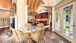 A spacious dining area with a round glass table and wicker chairs, a fireplace, and a view of the kitchen and outdoor area through large windows. - Lovely Brookfield Home w/ Private Deck & Views (Brookfield)