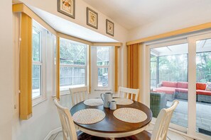 A dining area with a round table, four chairs, and a pitcher. There are windows with curtains, a view of the outside patio, and framed pictures on the wall. - Pet-Friendly Home w/ Pool, Close to Venice Beaches (Venice)