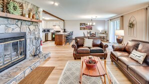 A spacious living room with a stone fireplace, leather sofas, and a dining area with a kitchen in the background. - Newly Renovated Sky Valley Condo w/ Mtn Views (Sky Valley)