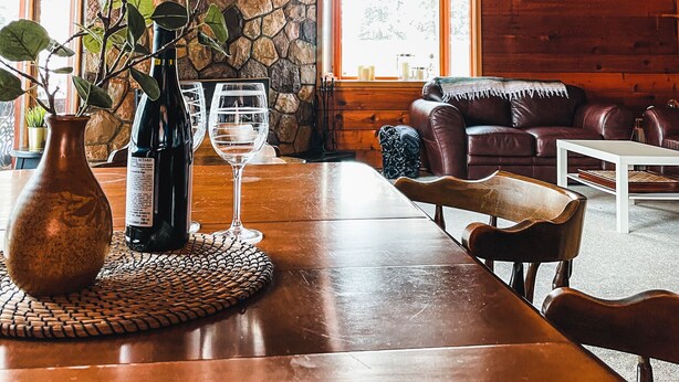 Un intérieur en bois avec un mur en pierre, une table à manger agrémentée d’un vase et de verres à vin, un canapé en cuir et un ventilateur de plafond.
