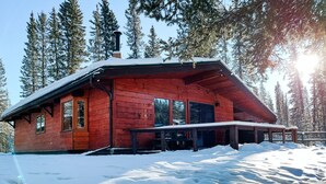 Une cabane en bois dotée d’un porche abrité, entourée de neige et de grands pins.