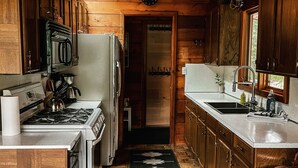 Une cuisine rustique aménagée dans une cabane en bois, avec un poêle, un réfrigérateur, un évier et des placards en bois.
