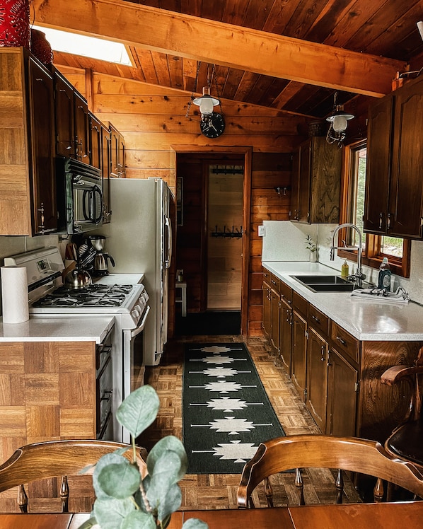 A wooden cabin kitchen with a stove, refrigerator, sink, and wooden cabinets.