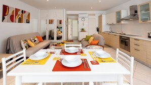 Un apartamento moderno con comedor para cuatro personas, cocina con electrodomésticos de acero inoxidable y sala de estar con sofá y cojines.